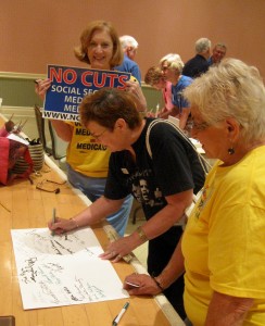 Villagers Sue Azia (left) and Sue Michalson (right) assist Villager Linda Hobbs as she signs a Medicare "birthday card."