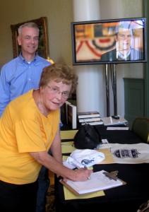 Helen Jacker of the Village of Del Mar signs a petition at the Defend America event as speaker Steve Russell looks on.