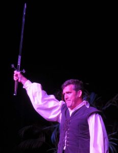 Patrick Ryan Sullivan raises his sword to the sky as King Arthur. 