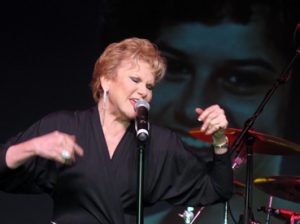 Peggy March sings in front of her teenage image on screen.