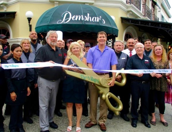 Gary Lester of The Villages Lake Sumter Inc. uses the big scissors to cut the ribbon at Demshar's.
