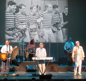 The Beach Boys sing at The Sharon with a video of the band from the 1960s. Mike Love is on the right singing and long time band member Bruce Johnston plays keyboards.