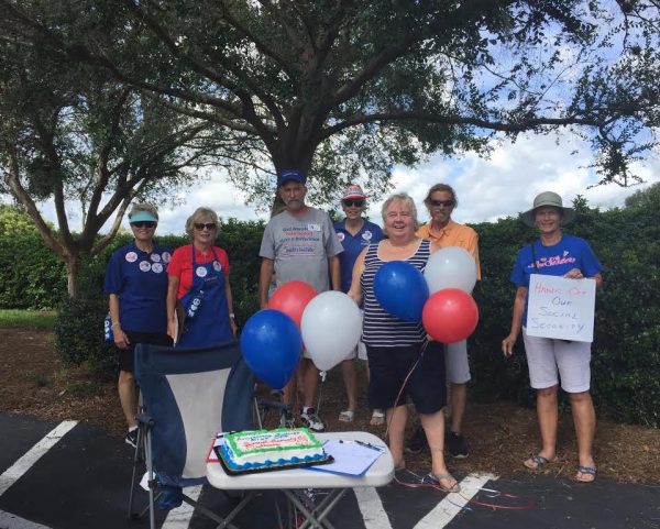 Cindy Lenhart and attendants present their cake to celebrate Medicare and Social Security's birthdays in front of Congressman Webster's Villages office.