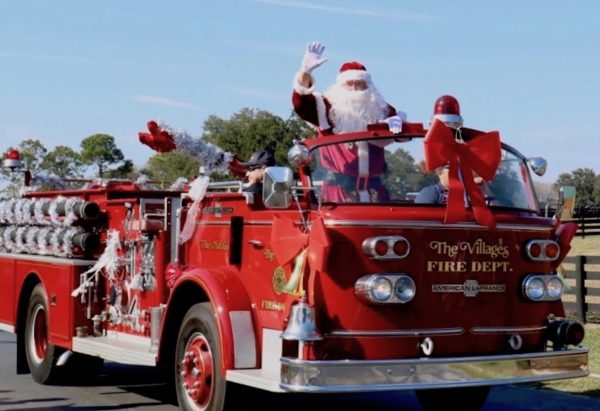 Santa Claus waves while riding in a vintage firetruck